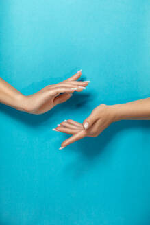 Crop anonymous woman holding hands with perfect manicure gracefully against bright blue background - ADSF29723