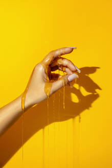Crop unrecognizable female showing hand with manicure and aromatic honey fluids on yellow background with shade - ADSF29724
