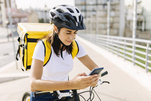 Auslieferungsfrau, die ihr Handy überprüft, während sie mit dem Fahrrad auf der Straße steht - XLGF02238