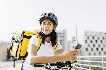 Lächelnde Zustellerin mit Mobiltelefon, die sich auf einen Fahrradgriff stützt - XLGF02239