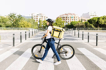 Frau mit Rucksack und Fahrrad auf der Straße an einem sonnigen Tag - XLGF02242