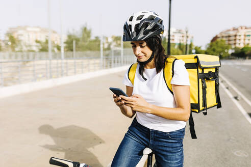 Weiblicher Zusteller mit Fahrrad und Mobiltelefon an einem sonnigen Tag - XLGF02243