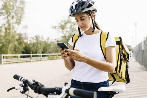 Weiblicher Zusteller, der ein Mobiltelefon benutzt, während er mit dem Fahrrad auf der Straße steht - XLGF02248