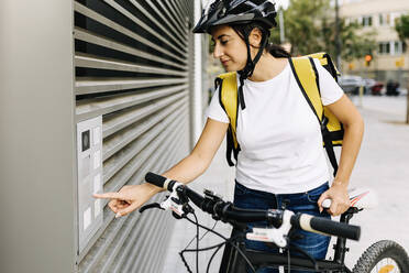 Delivery woman opening gate while standing by bicycle - XLGF02254