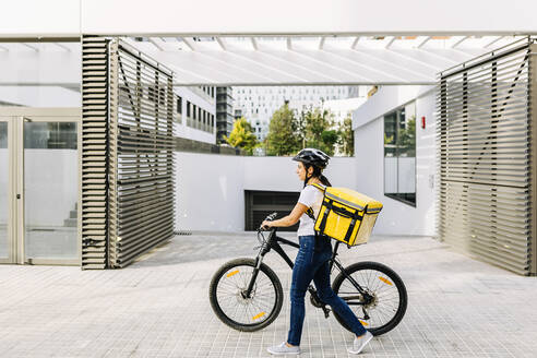 Weiblicher Zusteller mit Fahrrad auf dem Fußweg - XLGF02256