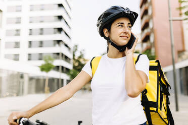 Delivery woman talking on mobile phone in city - XLGF02259