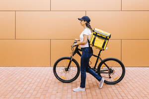 Lieferfrau mit Rucksack, die auf dem Fußweg Fahrrad fährt - XLGF02267