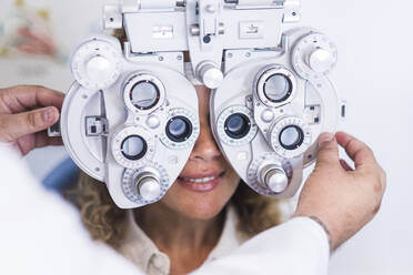 Ein männlicher Optometrist untersucht eine Patientin durch den Phoropter - SIPF02343