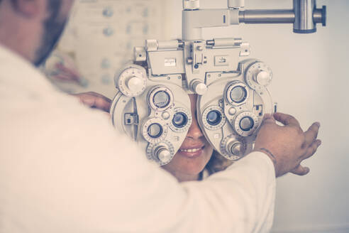 Männlicher Augenarzt, der die Sehkraft eines Patienten durch einen Phoropter in der Klinik untersucht - SIPF02344