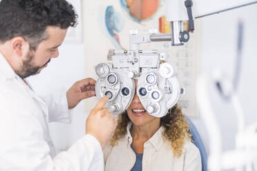 Male optometrist adjusting phoropter while checking female patient's eyesight - SIPF02345