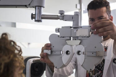 Männliche Fachkraft stellt den Phoropter bei der Untersuchung eines Patienten in der Klinik ein - SIPF02347