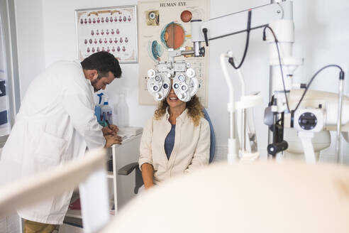 Männlicher Arzt schreibt in ein Buch, während er einen Patienten in einer Klinik untersucht - SIPF02348