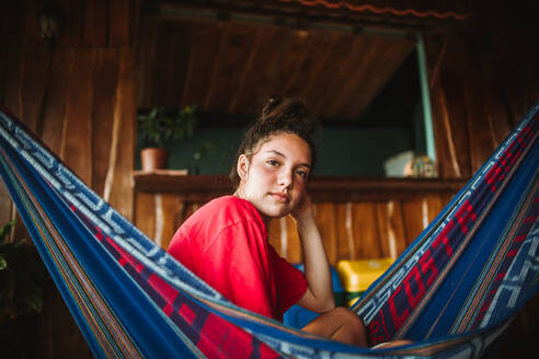 Side view of serene young female traveler in bikini looking at camera chilling in hammock hanging on terrace of tropical house during summer holidays in Uvita town in Costa Rica - ADSF29753