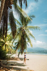 Seitenansicht einer nicht erkennbaren Frau in Badekleidung, die ihren Sommerurlaub am malerischen Strand mit tropischen Palmen und Sandstrand in der Stadt Uvita in Costa Rica genießt - ADSF29756
