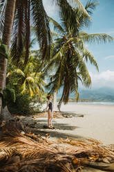 Seitenansicht einer nicht erkennbaren Frau in Badekleidung, die ihren Sommerurlaub am malerischen Strand mit tropischen Palmen und Sandstrand in der Stadt Uvita in Costa Rica genießt - ADSF29757