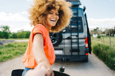 Glückliche afroamerikanische Frau mit Longboard, die lächelt und in die Kamera schaut, während sie einen Erntefreund während einer Autoreise zum Van führt - ADSF29802