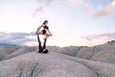 Serene woman balancing in King Pigeon pose on legs of man while practicing acroyoga in highlands - ADSF29831