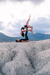 Seitenansicht einer anmutigen Frau, die auf den Beinen eines Mannes balanciert, während einer Acroyoga-Sitzung in den Bergen - ADSF29832