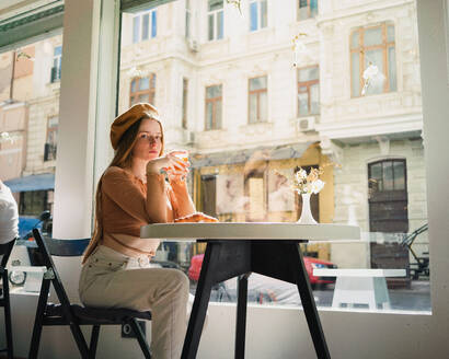 French female in beret sitting at table in cafe with aromatic glass of coffee and freshly baked croissant - ADSF29833