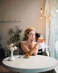 Französin mit Baskenmütze sitzt am Tisch in einem Café mit einem aromatischen Glas Kaffee und einem frisch gebackenen Croissant - ADSF29835