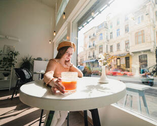 Französin mit Baskenmütze sitzt am Tisch in einem Café mit einem aromatischen Glas Kaffee und einem frisch gebackenen Croissant - ADSF29836