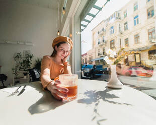 Französin mit Baskenmütze sitzt am Tisch in einem Café mit einem aromatischen Glas Kaffee und einem frisch gebackenen Croissant - ADSF29837