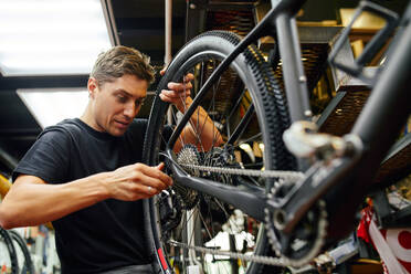 Männlicher Techniker, der ein Rad an einem Fahrrad befestigt, während er in einer modernen Fachwerkstatt arbeitet - ADSF29931