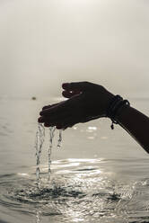 Crop gesichtslose Frau mit einer Handvoll Wasser in nassen Händen im Meer am Morgen in Alcudia - ADSF29947