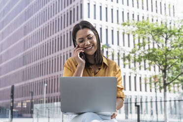 Lächelnde Geschäftsfrau, die mit einem Smartphone spricht, während sie im Büropark arbeitet - PNAF02167