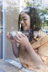 Glückliche junge Geschäftsfrau beim Kaffeetrinken im Café - PNAF02180