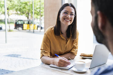 Lächelnde Geschäftsfrau sieht Mann bei der Arbeit im Café an - PNAF02183