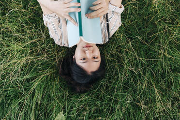 Woman holding book while lying on grass - ASGF01381