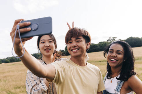 Lächelnde Freunde nehmen Selfie durch Handy im Park - ASGF01390