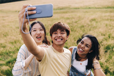 Freunde lächelnd bei der Aufnahme eines Selfies mit dem Handy im Park - ASGF01392