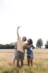 Mann nimmt Selfie mit Frauen durch Handy auf Wiese - ASGF01393