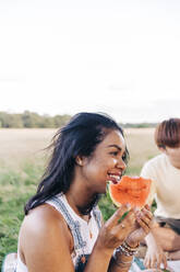 Smiling woman holding watermelon slice during picnic at park - ASGF01403