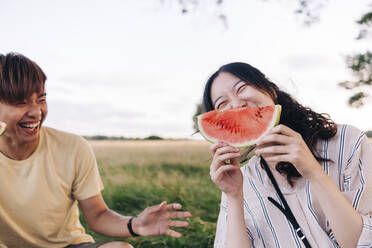 Fröhliche Frau, die mit einem Freund im Park eine Wassermelone isst - ASGF01405