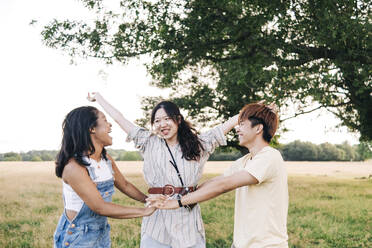 Woman with arms outstretched looking at friends while playing on meadow - ASGF01415