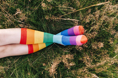 Woman wearing rainbow socks with legs crossed at ankle on grass - ASGF01427