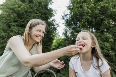Lächelnde Mutter füttert ihre Tochter mit Erdbeeren im Hinterhof - LLUF00004