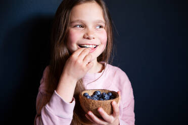 Smiling girl picking fresh blueberries on dark background - CAVF94662