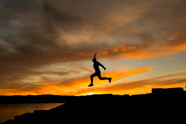 Silhouette eines springenden Mannes mit Mütze im Sonnenuntergang - CAVF94686