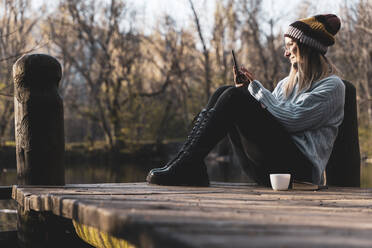 Women relaxing in the wooden pier lake with smartphone. - CAVF94710