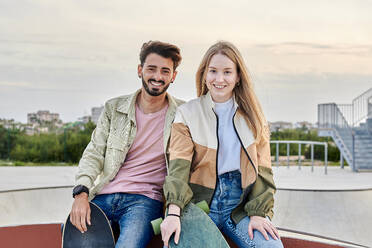 Young multiracial couple looks at the camera smiling in a skate park - CAVF94797