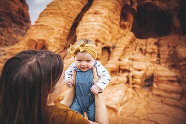 Eine junge Frau mit einem Baby steht in der Nähe von roten Felsen im Valley of Fire - CAVF94798