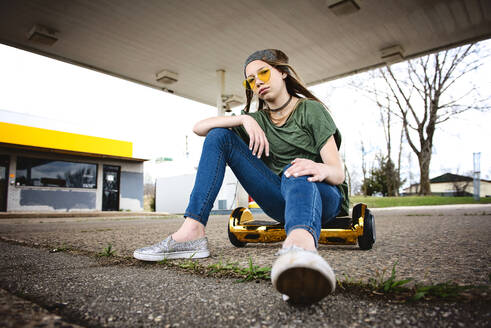 Cool tween girl with blond hair and sunglassess sitting on hoverboard - CAVF94825