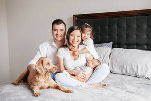 Glückliche multirassische junge Familie mit Kindern und Hund auf dem Bett. - CAVF94828