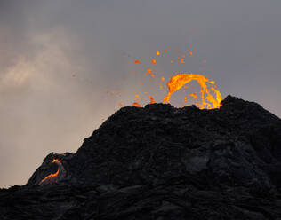 Orangefarbene Lava über dem Fuhrwerk eines ausbrechenden Vulkans bei Sonnenuntergang - CAVF94839