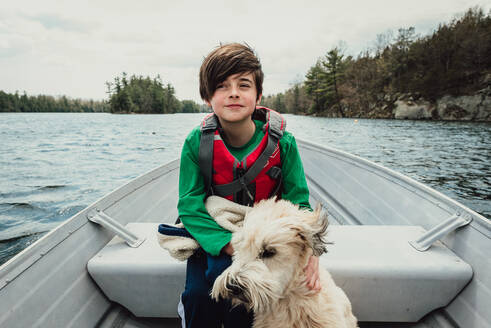 Young boy and dog sitting in a metal boat travelling on a lake. - CAVF94869