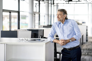 Mature male professional with hands clasped looking away at office - PESF03167